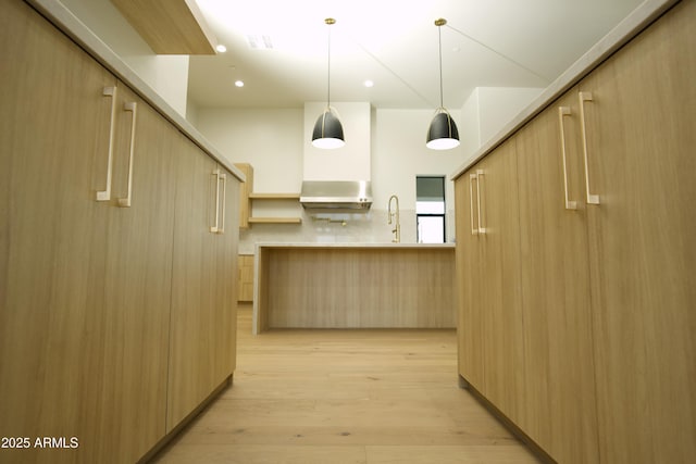 kitchen with light brown cabinetry, hanging light fixtures, ventilation hood, and light hardwood / wood-style flooring