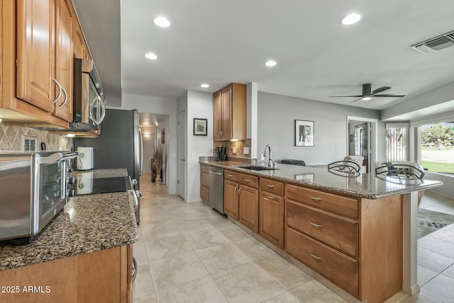 kitchen with tasteful backsplash, a peninsula, brown cabinetry, stainless steel appliances, and a sink