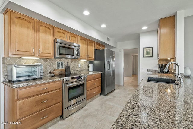 kitchen with a toaster, decorative backsplash, dark stone countertops, appliances with stainless steel finishes, and a sink