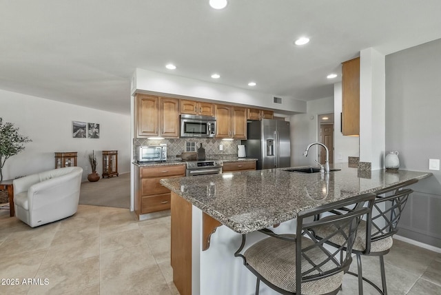 kitchen with a kitchen bar, a sink, dark stone countertops, backsplash, and appliances with stainless steel finishes