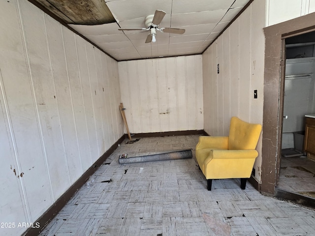 unfurnished room with a ceiling fan, wood walls, and baseboards