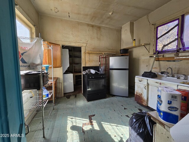 kitchen with light floors, black range with gas stovetop, freestanding refrigerator, a sink, and stacked washing maching and dryer