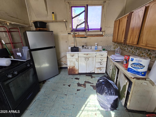 kitchen with freestanding refrigerator, light countertops, black gas stove, light floors, and a sink