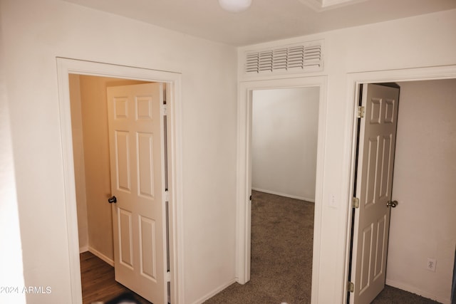 corridor with dark carpet, visible vents, and baseboards