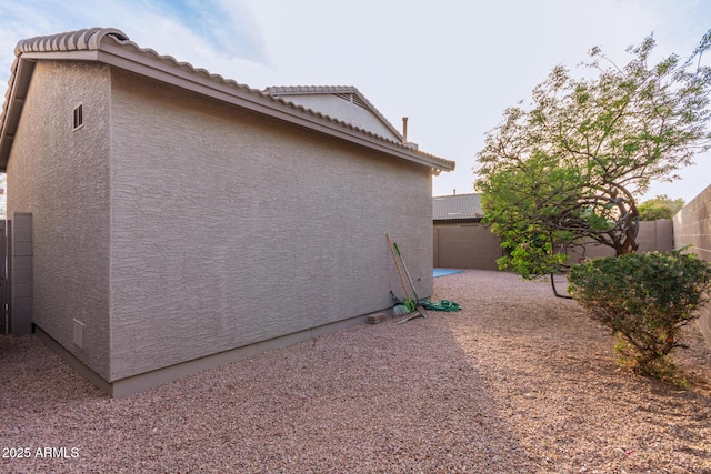 view of property exterior featuring a tiled roof, fence, and stucco siding