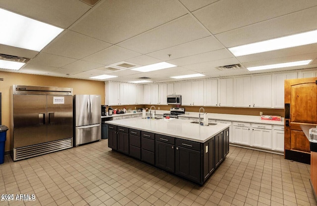 kitchen with appliances with stainless steel finishes, a sink, white cabinetry, light countertops, and a paneled ceiling
