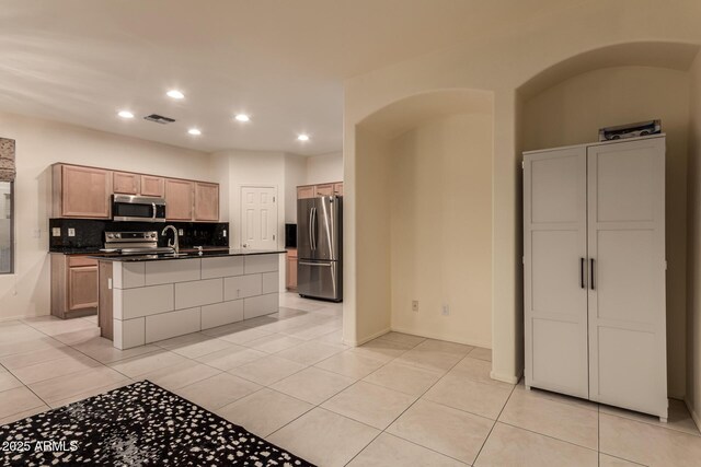 kitchen with stainless steel appliances, visible vents, tasteful backsplash, an island with sink, and dark countertops