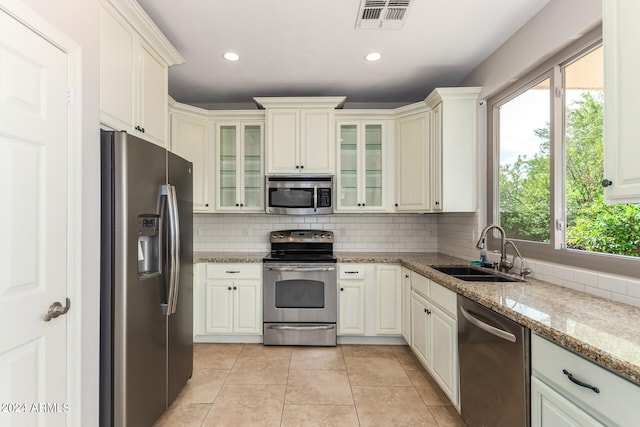 kitchen with appliances with stainless steel finishes, sink, light stone counters, and a wealth of natural light