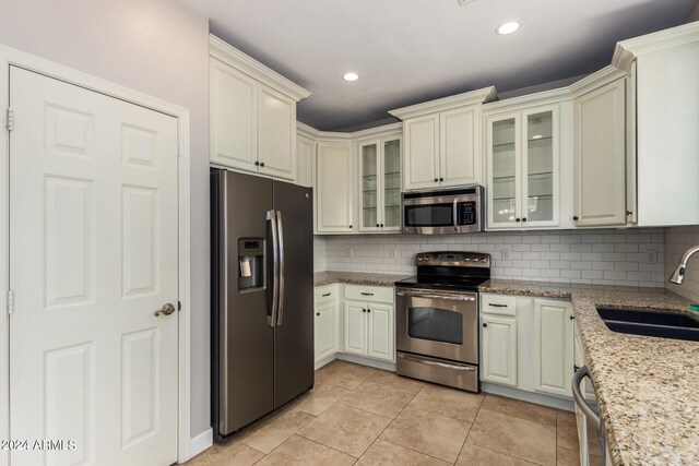 kitchen with sink, decorative backsplash, appliances with stainless steel finishes, light tile patterned floors, and light stone countertops