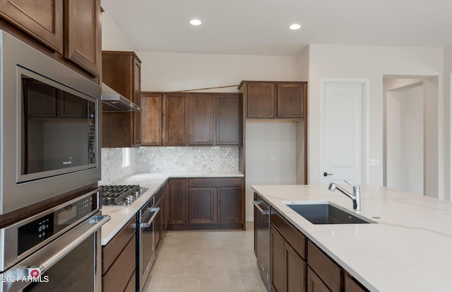 kitchen featuring appliances with stainless steel finishes, tasteful backsplash, light stone counters, exhaust hood, and sink