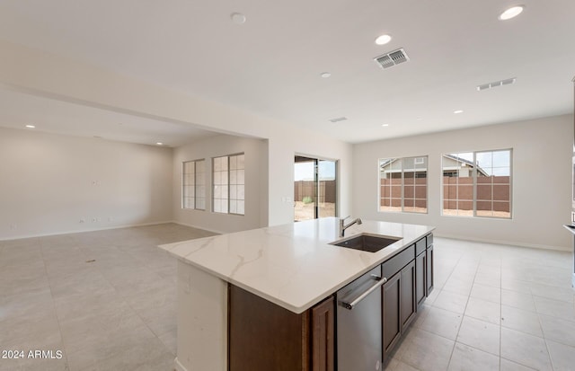 kitchen featuring dishwasher, a kitchen island with sink, sink, light stone countertops, and dark brown cabinets