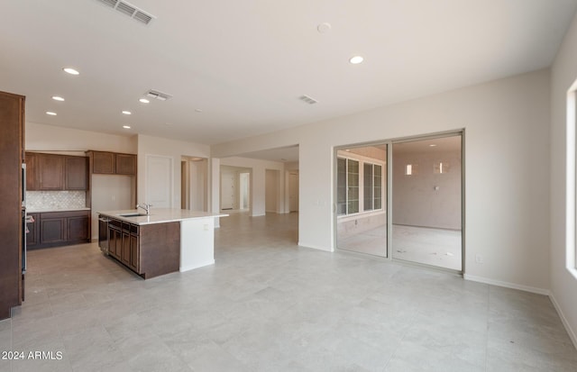 kitchen with tasteful backsplash, a center island with sink, wall oven, and sink