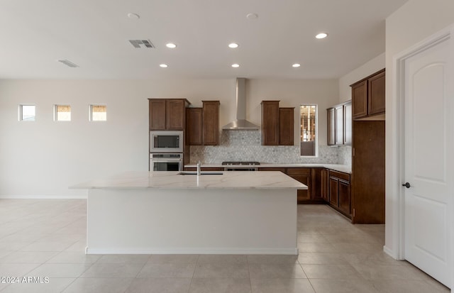 kitchen featuring light stone countertops, sink, wall chimney exhaust hood, stainless steel appliances, and an island with sink