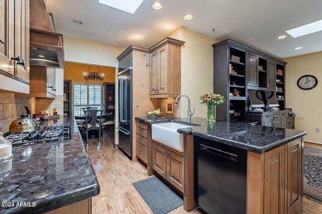 kitchen with dishwasher, stainless steel gas cooktop, sink, light wood-type flooring, and a skylight