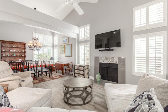 living room featuring ceiling fan with notable chandelier, light wood-type flooring, a towering ceiling, and a high end fireplace