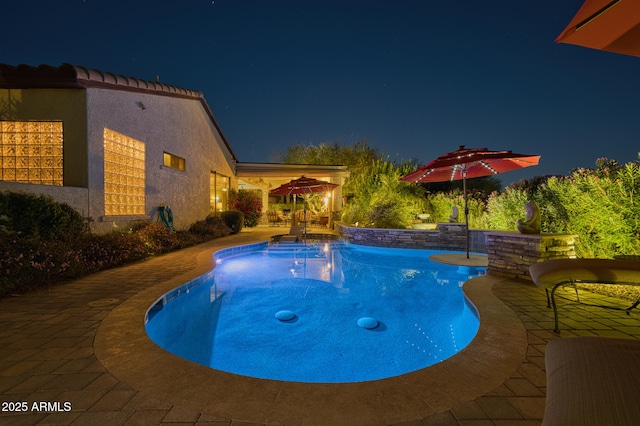 pool at night featuring a jacuzzi and a patio