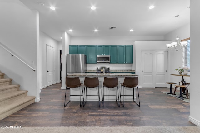 kitchen with appliances with stainless steel finishes, stone countertops, pendant lighting, a kitchen bar, and a kitchen island with sink