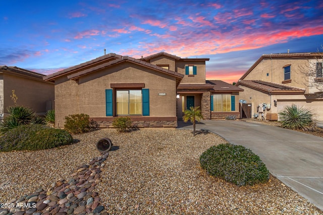 view of front of property featuring stone siding, stucco siding, a tiled roof, and concrete driveway