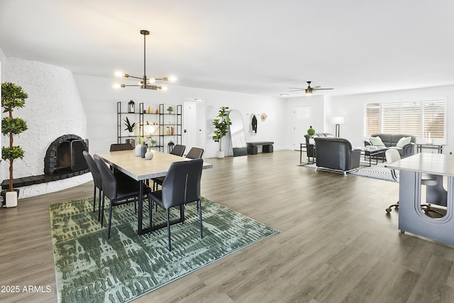 dining space with a fireplace, wood finished floors, and ceiling fan with notable chandelier