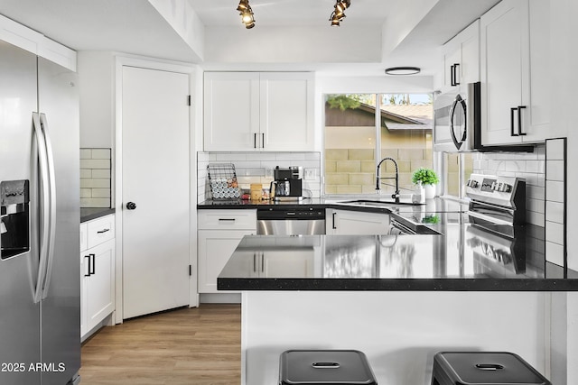 kitchen featuring stainless steel appliances, a peninsula, a sink, and dark countertops