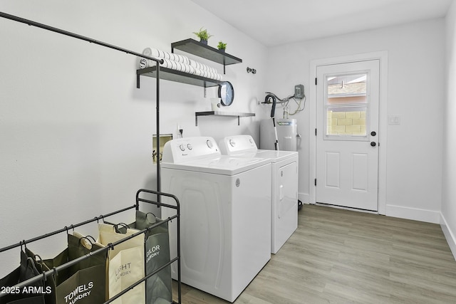 clothes washing area featuring washing machine and clothes dryer, light wood-style flooring, baseboards, water heater, and laundry area