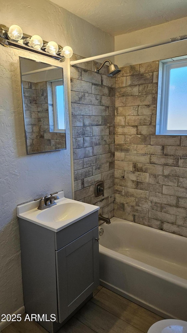 bathroom with a textured wall, wood finished floors, bathtub / shower combination, and vanity
