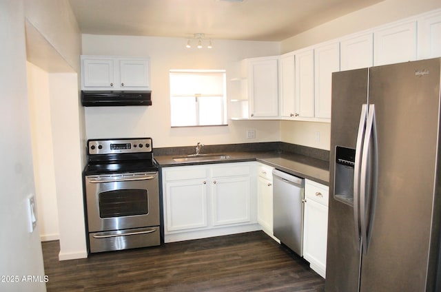 kitchen featuring appliances with stainless steel finishes, a sink, extractor fan, dark countertops, and white cabinetry