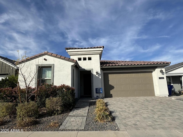 mediterranean / spanish-style home featuring a garage, a tiled roof, decorative driveway, and stucco siding