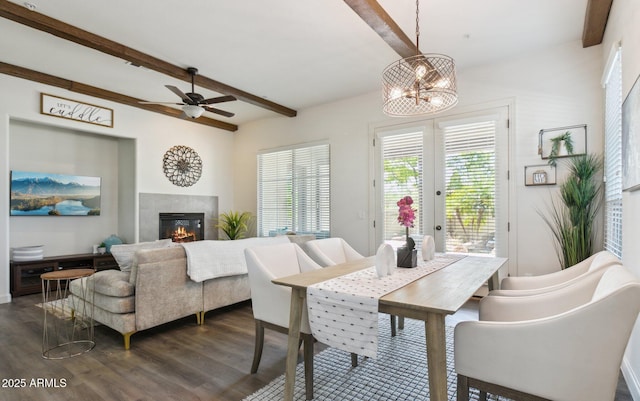 dining space featuring beamed ceiling, dark wood-style flooring, a chandelier, ceiling fan, and a tile fireplace