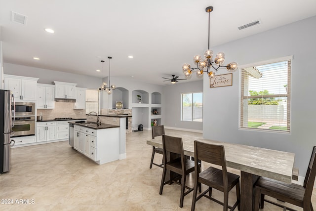 kitchen with stainless steel appliances, a kitchen island with sink, sink, tasteful backsplash, and decorative light fixtures