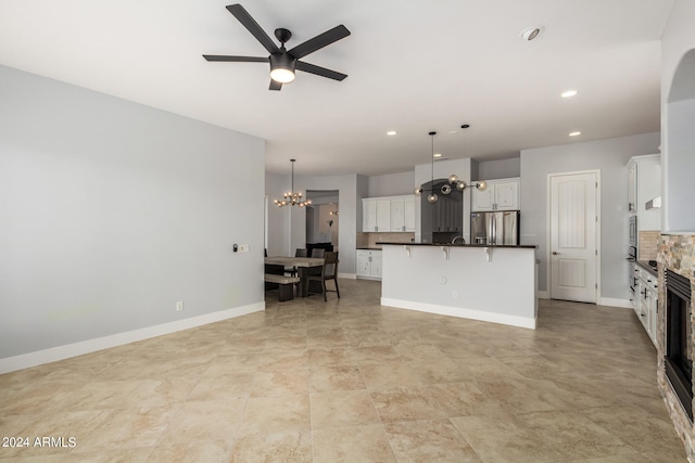 kitchen with a center island with sink, ceiling fan with notable chandelier, stainless steel fridge with ice dispenser, white cabinets, and decorative light fixtures