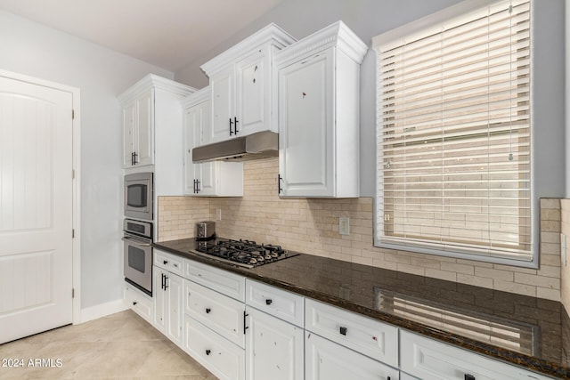 kitchen featuring appliances with stainless steel finishes, white cabinets, light tile patterned flooring, backsplash, and dark stone counters