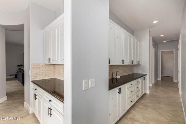 kitchen featuring decorative backsplash, light tile patterned flooring, white cabinets, and dark stone counters