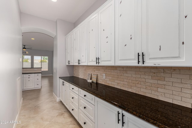 kitchen featuring dark stone counters, white cabinets, light tile patterned floors, and ceiling fan