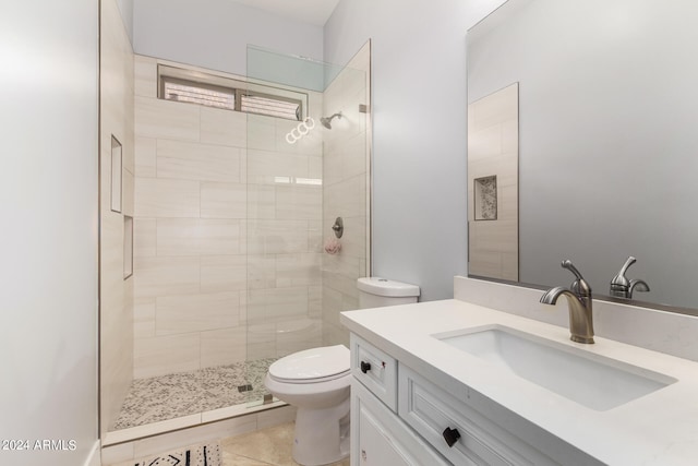 bathroom with toilet, a tile shower, vanity, and tile patterned flooring