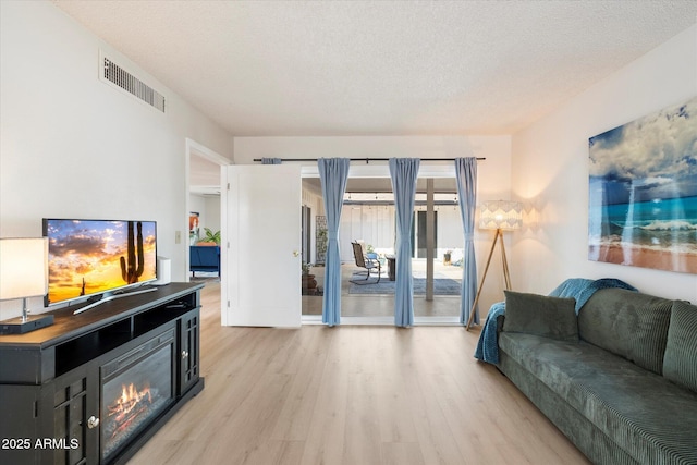 living room with visible vents, light wood-style floors, and a textured ceiling