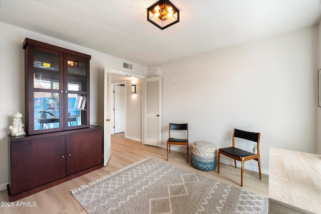 living area with visible vents, a textured ceiling, baseboards, and wood finished floors