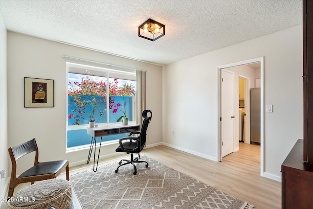 office area featuring baseboards, light wood-type flooring, and a textured ceiling