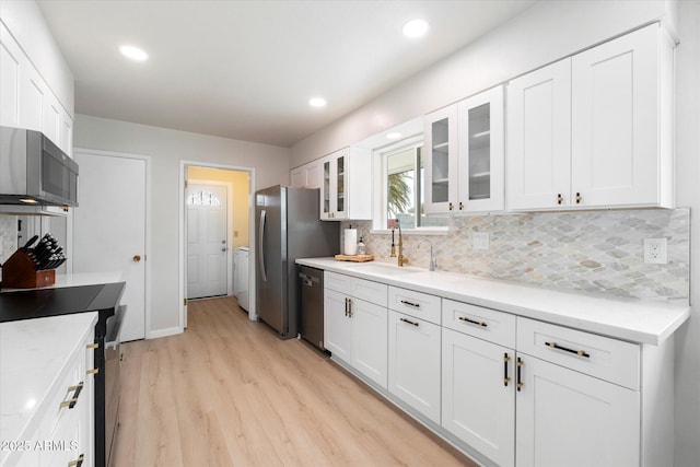 kitchen featuring a sink, tasteful backsplash, stainless steel appliances, white cabinets, and light wood finished floors