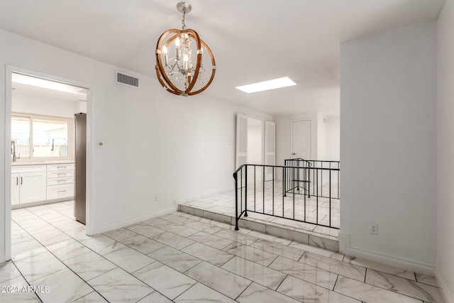 spare room with a skylight, visible vents, baseboards, marble finish floor, and an inviting chandelier