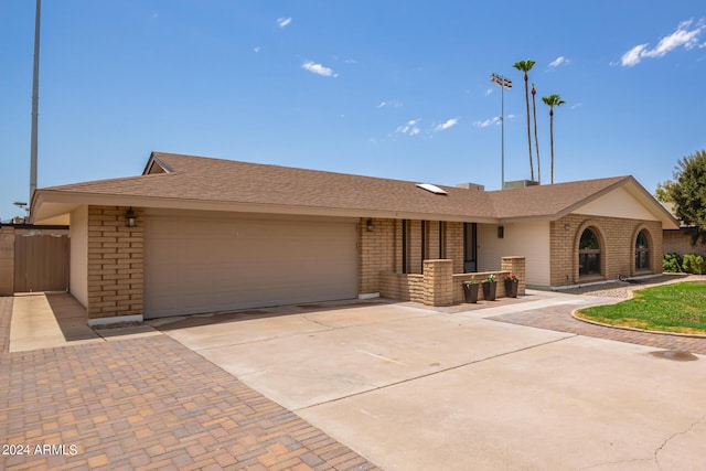 single story home with a garage, driveway, roof with shingles, fence, and brick siding