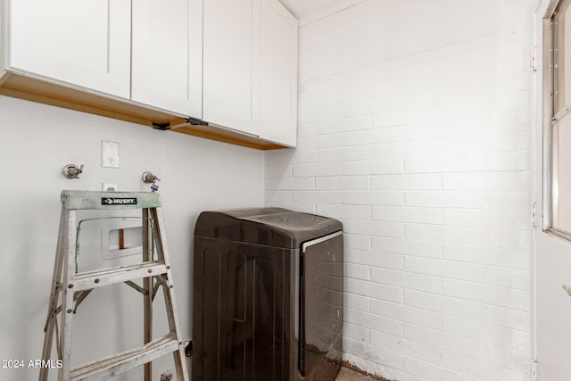 clothes washing area with brick wall and cabinet space