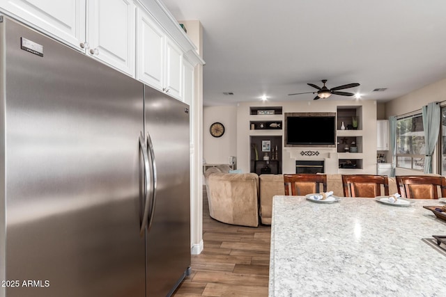 kitchen featuring visible vents, a fireplace, stainless steel fridge, white cabinets, and a ceiling fan