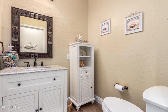 bathroom with toilet, baseboards, wood finished floors, and vanity