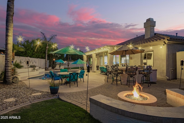 patio terrace at dusk featuring fence, outdoor dry bar, and an outdoor fire pit
