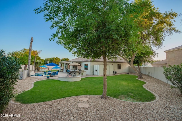 rear view of house with stucco siding, a fenced backyard, a fenced in pool, a patio area, and a lawn