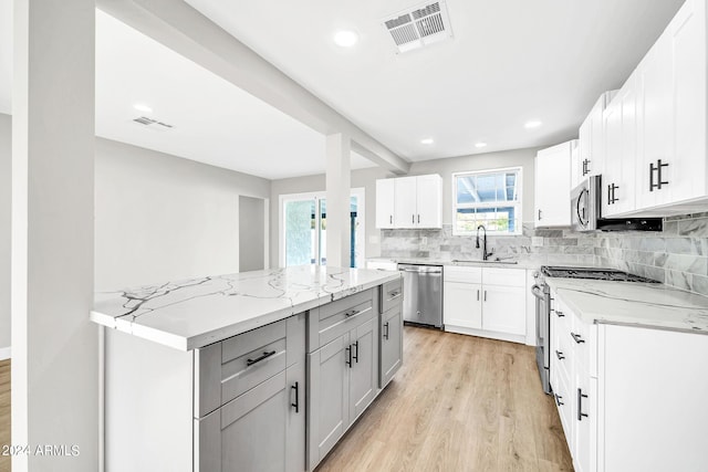 kitchen featuring white cabinets, appliances with stainless steel finishes, tasteful backsplash, light hardwood / wood-style floors, and light stone counters