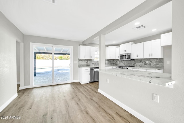 kitchen featuring backsplash, light stone countertops, light hardwood / wood-style floors, white cabinetry, and stainless steel appliances