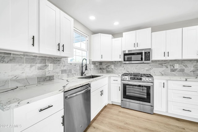 kitchen with sink, light wood-type flooring, light stone counters, white cabinetry, and stainless steel appliances