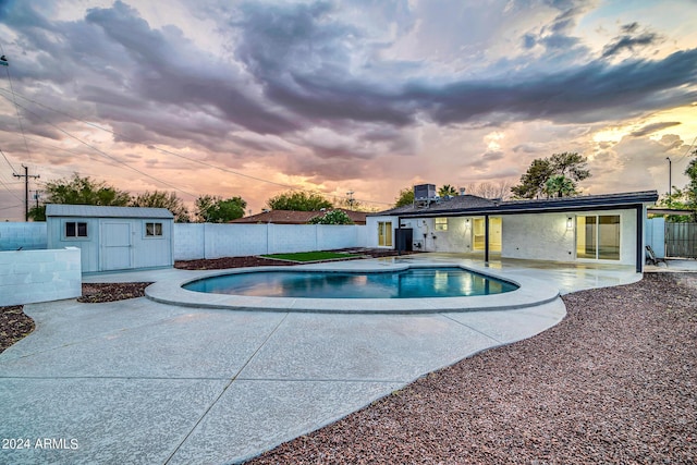 pool at dusk featuring a patio and a storage shed